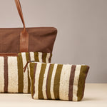 Artisan hand woven Cristina Pouch and Soledad Weekender in Forest pattern. The Soledad Weekender is cropped out to the left side. The Cristina Pouch is centered. The Forest pattern has vertical olive green and beige stripes.