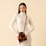 Hand woven artisan Eloisa Small Crossbody in Season Sparkle. A model wears the crossbody around her torso. The Eloisa Crossbody has embroidered detailing, a drawstring shape with orange tassels, and a leather strap.