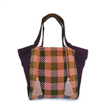 Hand woven artisan Rosa Tote in Moss Weave pattern. The Moss Weave is an orange, pink, and olive green grid plaid. The tote has dark purple triangular finishes and handles. It has two pale pink tassels attached with a leather cord.