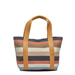 Front view of the Magali Tote in Blue Canyon. It has horizontal navy, orange, tan, beige, and light blue stripes. It has leather handles.