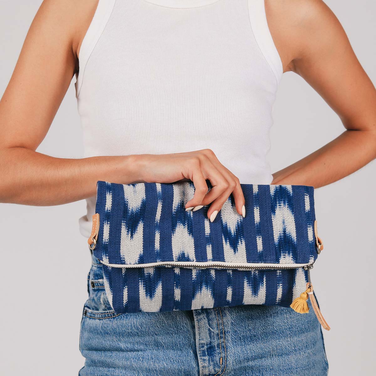 A model holds the hand woven artisan Florentina Clutch in her hand. It is in the Atitlán Hills pattern with a mini tassel and leather zipper pulls. 