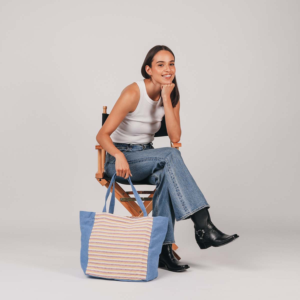 A model sits in a chair and holds the Blanca Tote in Cream Soda pattern.