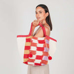 A model stands sideways and holds the handles of the artisan hand woven Rosa Tote in Raspberry Paleta.
