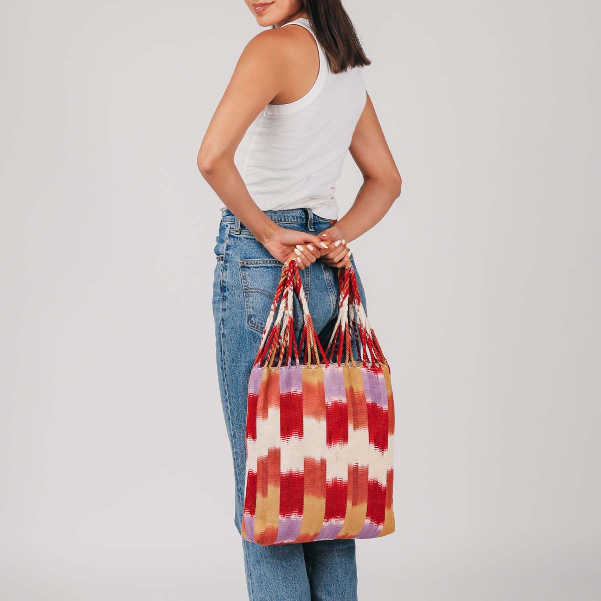 A model holds the hand woven artisan Apolonia Tote in Raspberry Paleta behind her back.