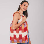 A model smiles at the camera and holds the hand woven artisan Apolonia Tote in Raspberry Paleta over her shoulder.