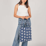 A model stands and holds the hand woven artisan Apolonia Tote in Atitlán Hills pattern.