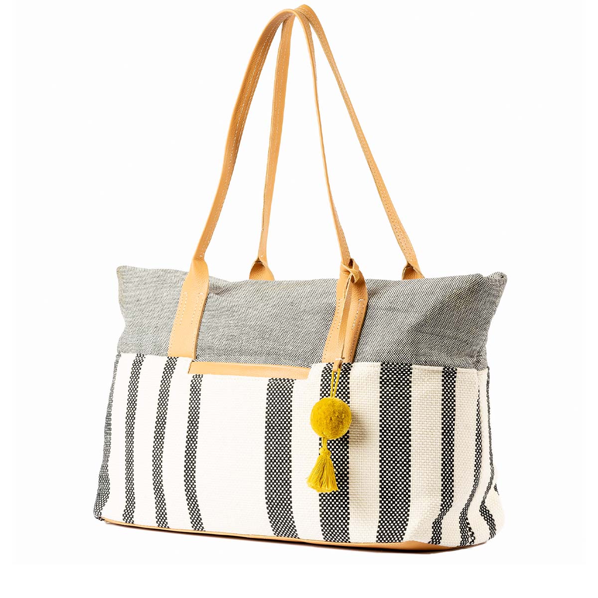 The Soledad Weekender in Tourmaline pattern shown at an angle.It has grey and white vertical stripes, leather handles, and a yellow pompom-tassel combination.
