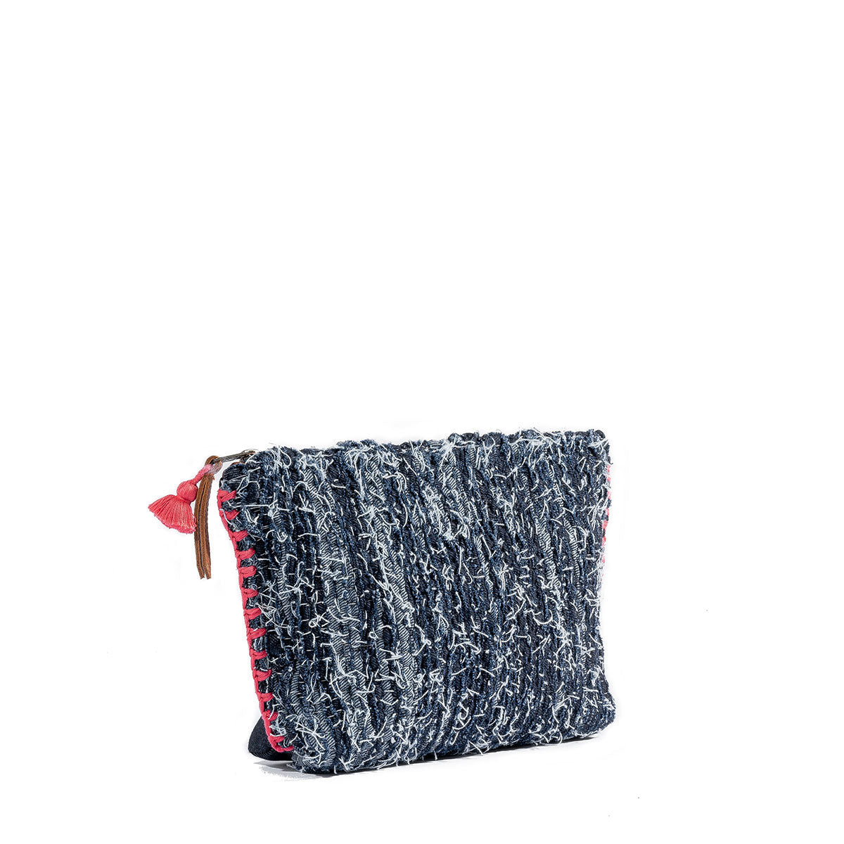A side angle of the artisan hand woven Cristina Cosmetic Pouch in Denimology. The Cristina Pouch has strips of denim woven together with thick coral pink visible side stitches. It has a coral pink mini tassel and a leather zipper pull.
