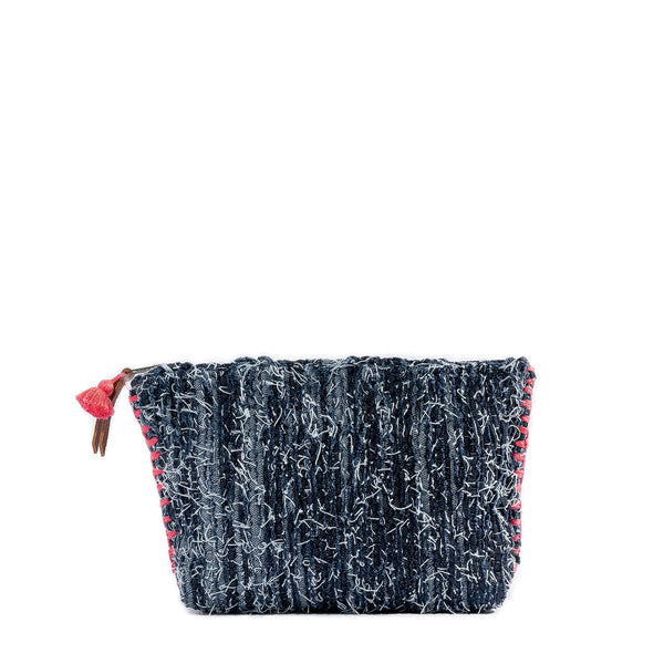 The front of the hand woven artisan Cristina Cosmetic Pouch in Denimology. The Cristina Pouch has strips of denim woven together with thick coral pink visible side stitches. It has a coral pink mini tassel and a leather zipper pull.