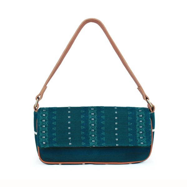 Olivia Artisan Handwoven Deep Forest Shoulder Bag. It has a deep turquoise and white geometric pattern. It has a leather strap and leather piping. The bag has a short and long width shape. It has a fabric fold over the top.