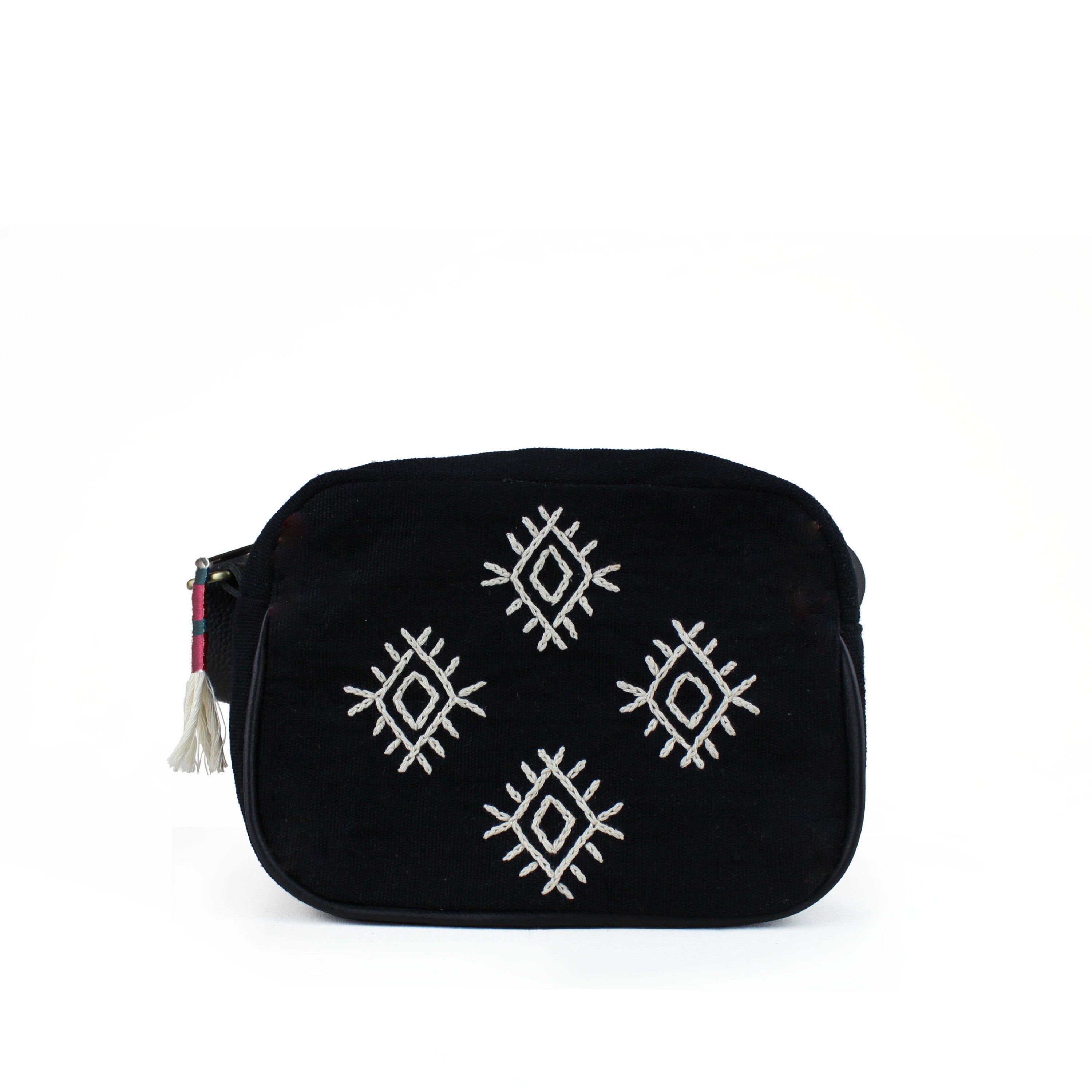 Artisan Juana Handwoven Diamond Embroidery Crossbody. The bag has a black background and four embroidered white diamonds. It has a woven red and green tassel attached to the zipper.