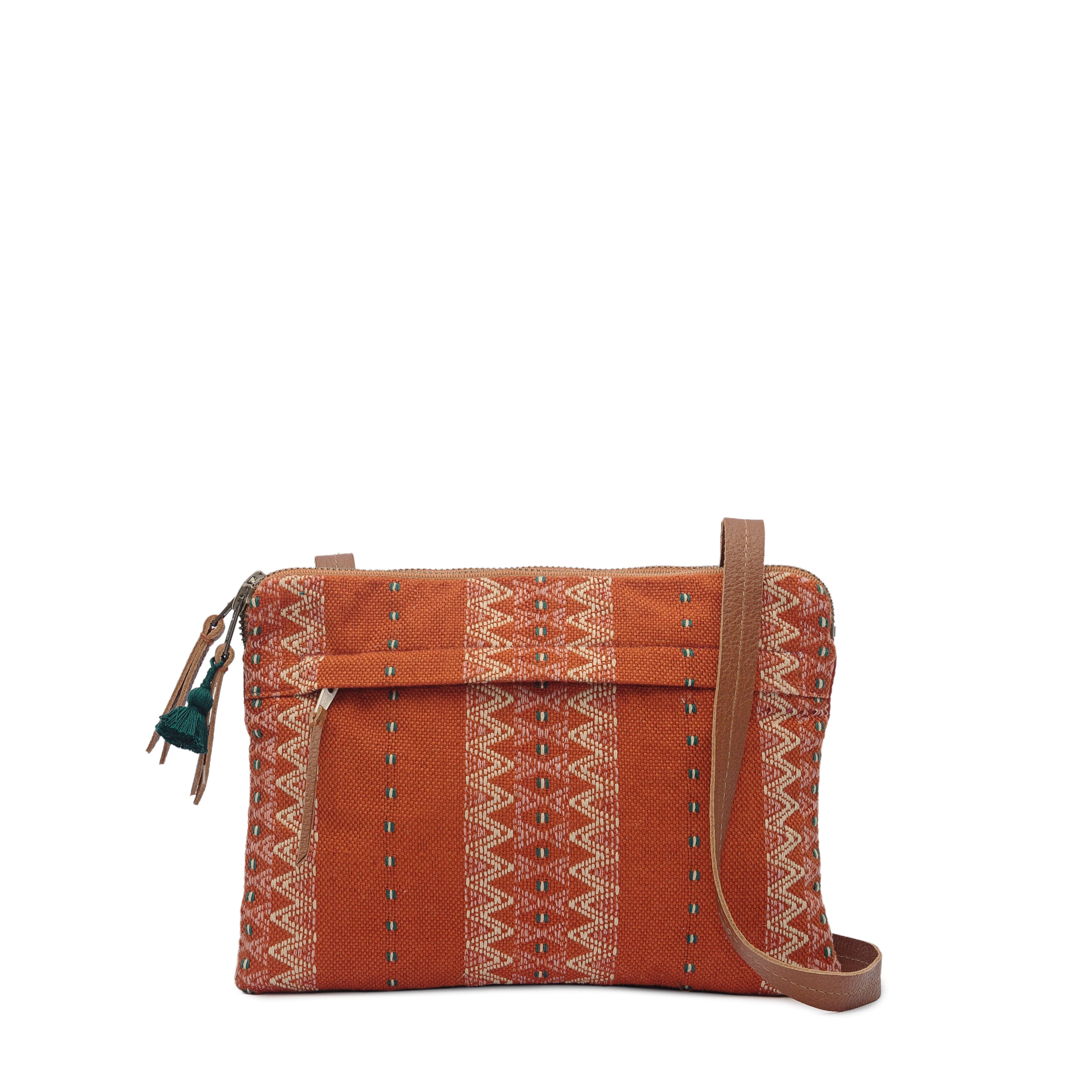 Artisan Miriam Handwoven Ginger Crossbody.  The fabric has a zigzag white pattern over an orange background. It has a phthalo green tassel and leather zipper pulls. It has a leather strap. 