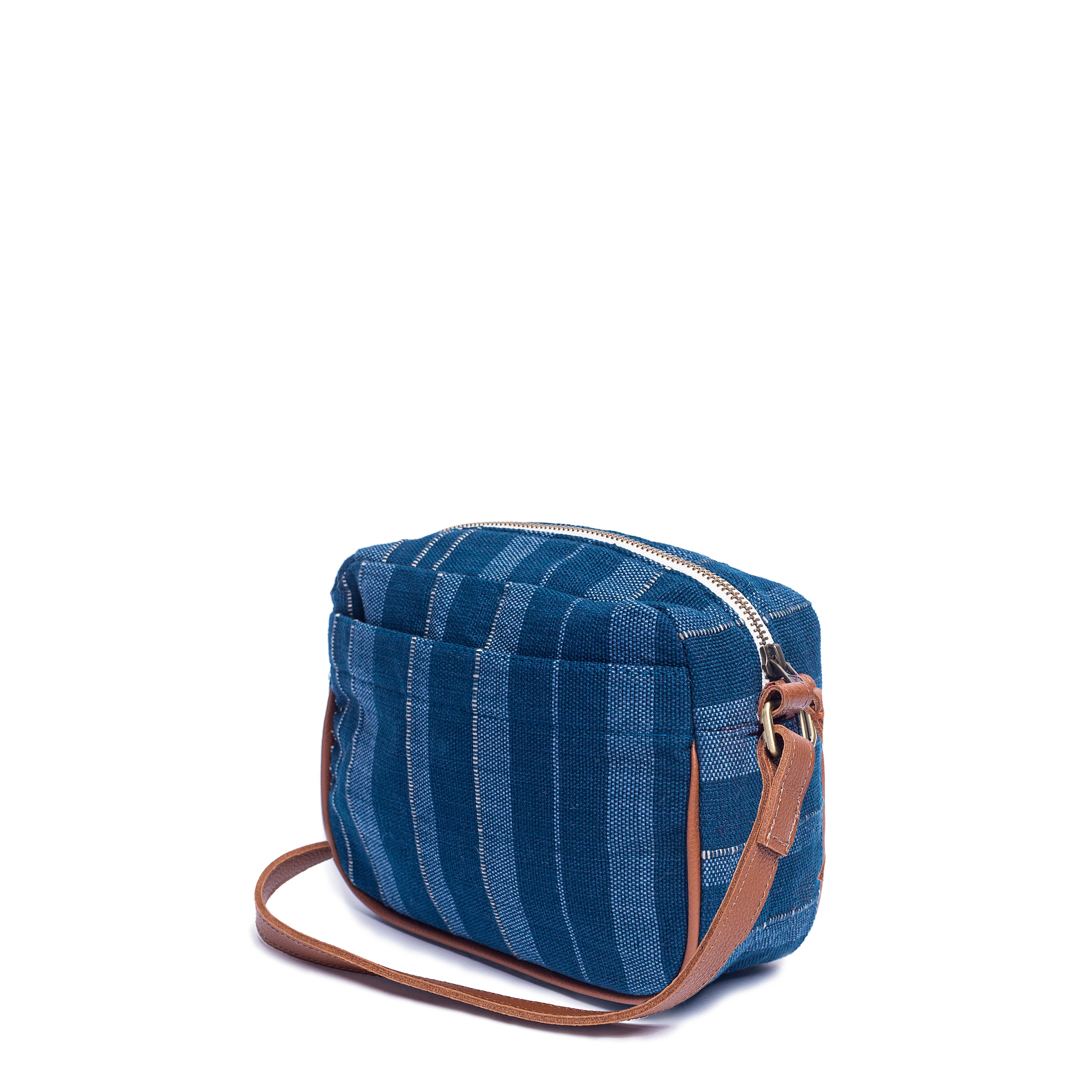 A side view of the hand woven artisan Juana Crossbody in Sky Haze. The Sky Haze pattern has vertical dark blue, lighter blue, and grey stripes. It has a leather vein detailing and leather strap. The top is closed by a zipper.