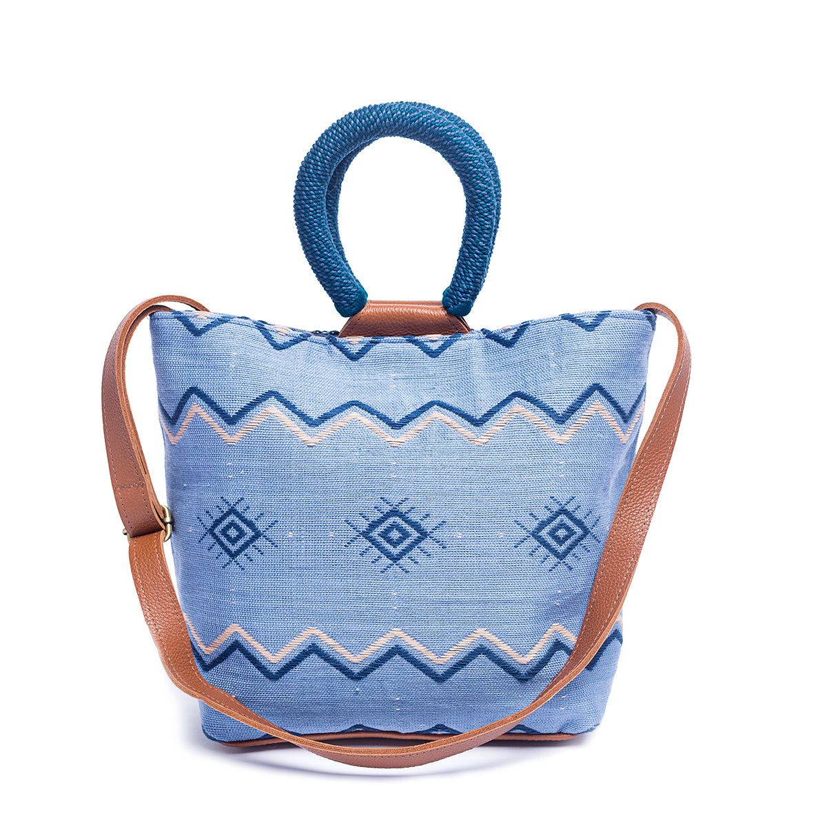 Front of the artisan Dalila Midi Handwoven Mountain Blue Tote. The tote has a bucket shape with rounded handles coiled in blue thread. The pattern has horizontal zigzag stripes and a diamond shape pattern in the middle section. The colors are light blue, dark blue, and white. It has an adjustable leather strap.