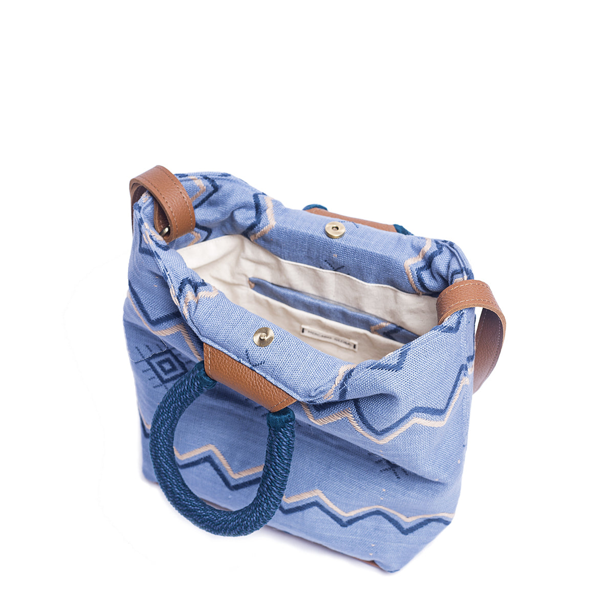 A top side view of the hand woven artisan Dalila Midi Tote in Mountain Blue. The interior has a white lining, an interior pocket, and a magnetic clasp.
