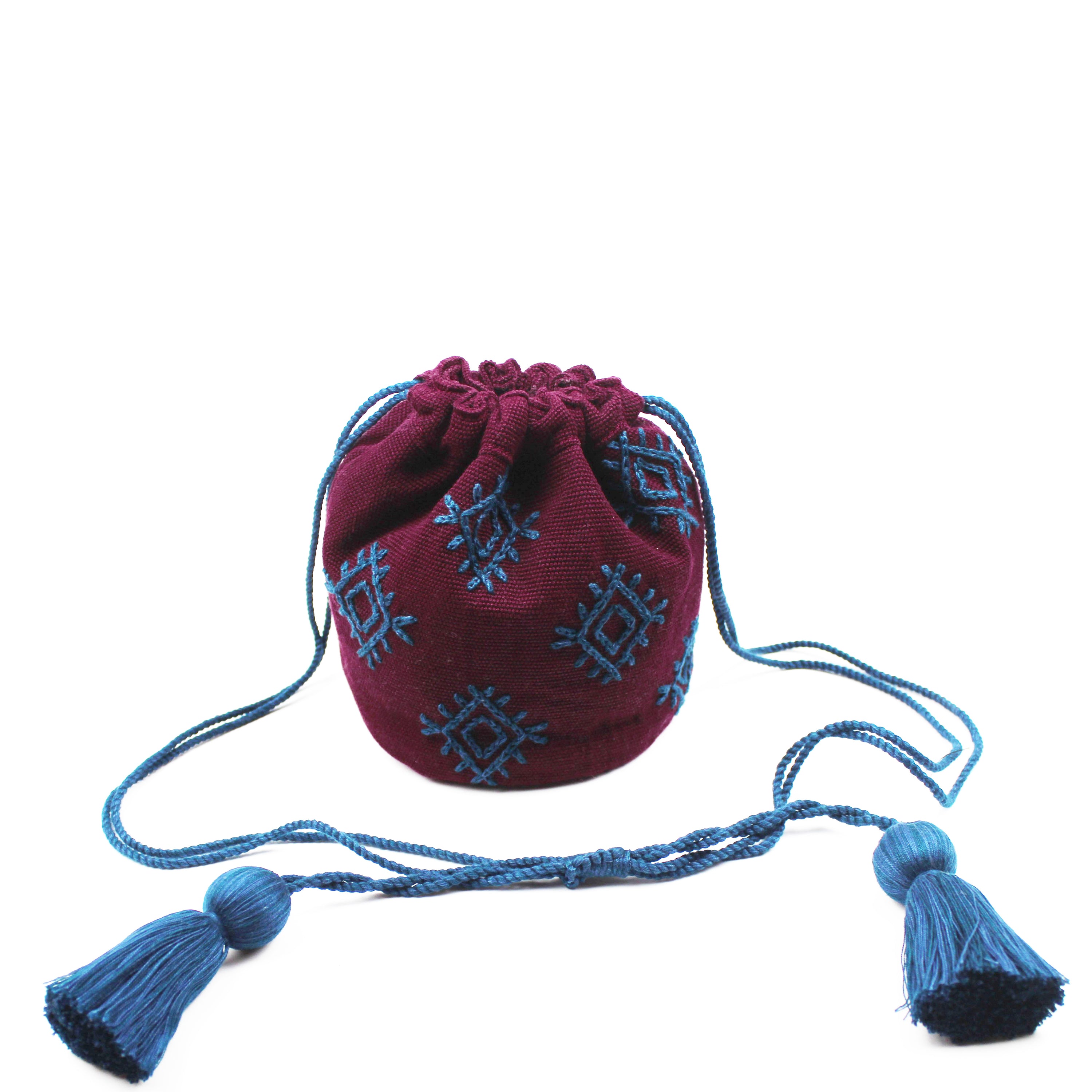 Hermelinda Handwoven Crossbody Mountain Dusk. The bucket bag is closed with a blue drawstring attached to tassels. The Mountain Dusk pattern has blue embroidered diamond shapes over a maroon background.