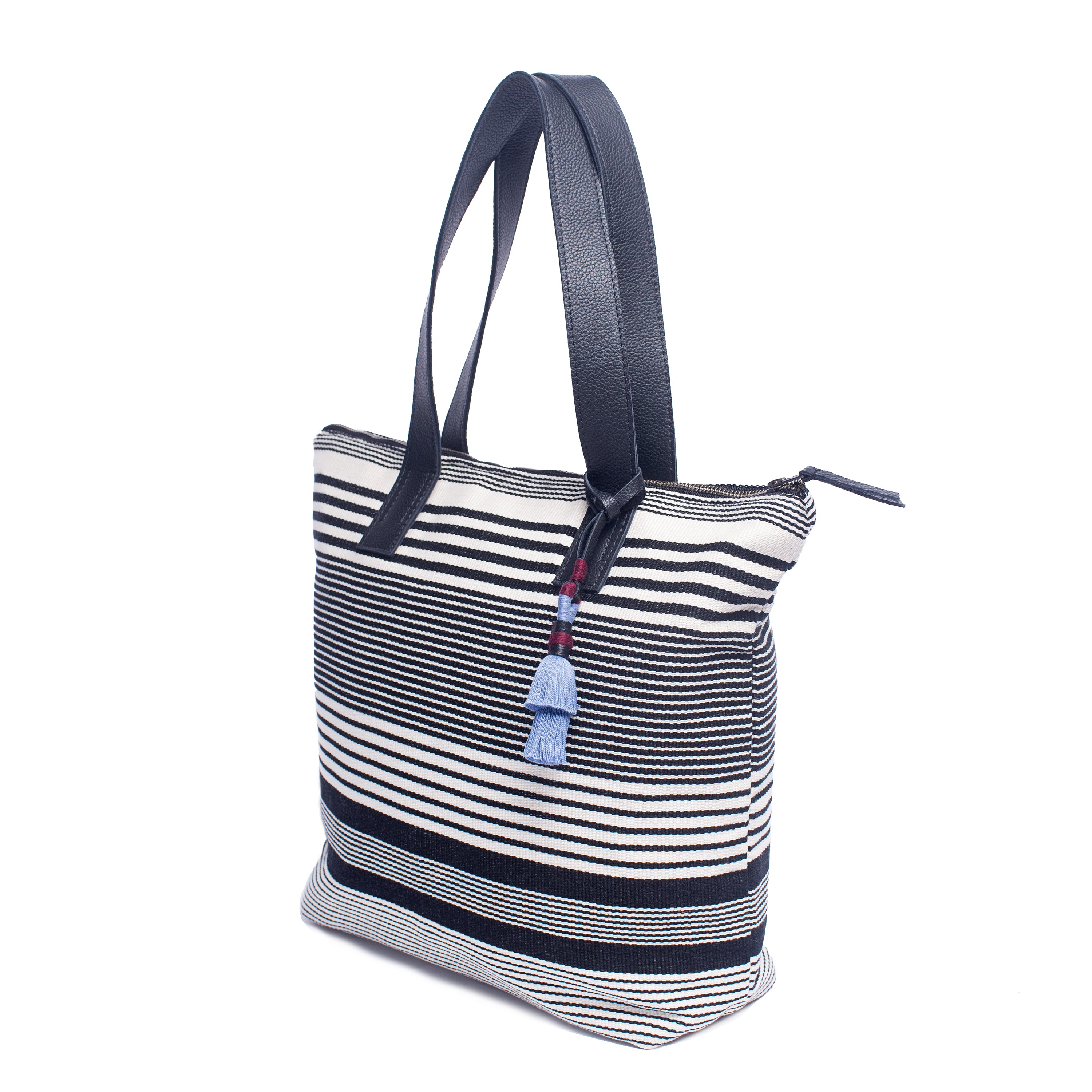 The right-sided angle of the Angela Tote in Black and White stripes. It has navy blue leather handles and a light blue tassel.