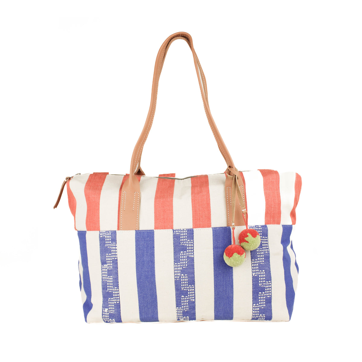 Hand woven artisan Soledad Weekender in Blueberry. The pattern has blue geometric stripes and orange stripes on the top fabric. It has leather handles. Attached are two orange and green pompoms with leather straps.