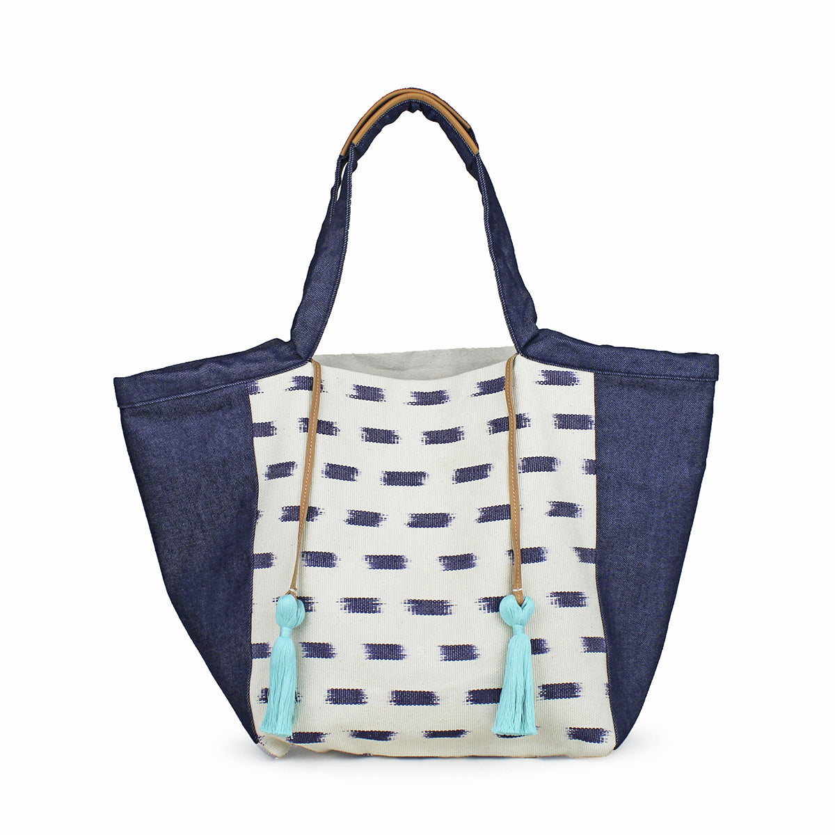 Artisan Rosa Handwoven Tote in Denim Jaspe. The center has an abstract blue square pattern over a white background. The sides have a dark denim wash fabric. The handles have leather detailing. It has two mint green tassels attached to leather cords.