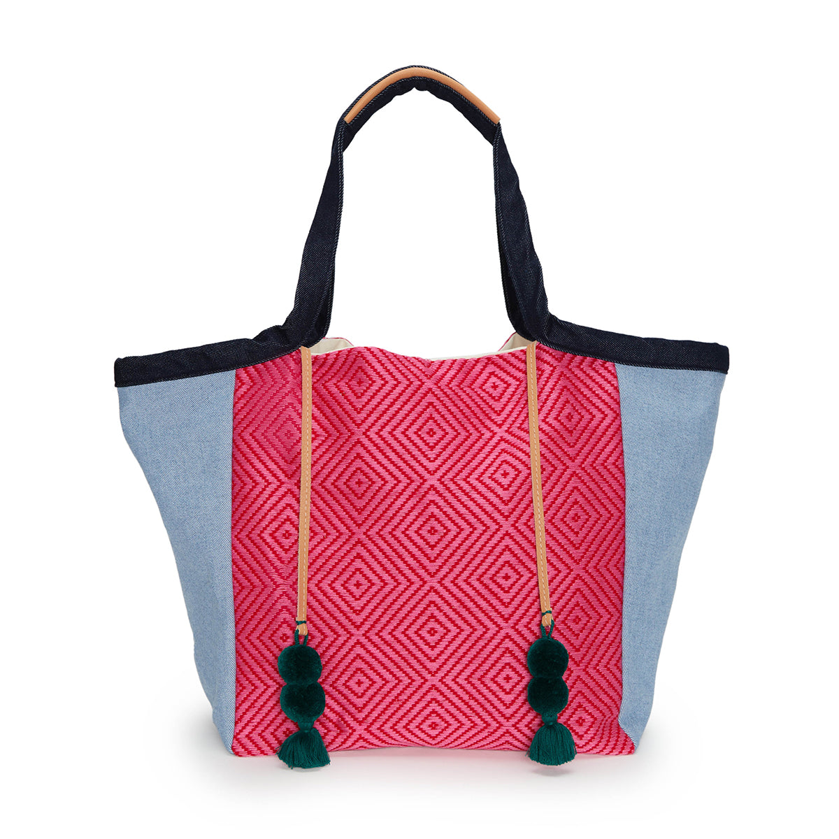 Artisan Rosa Hand Woven Tote in Raspberry. The Rosa has a diamond pink pattern in the center and light wash denim sides. It has dark green pompoms and tassels attached to leather cords. The hands have a dark wash denim fabric and leather detailing.