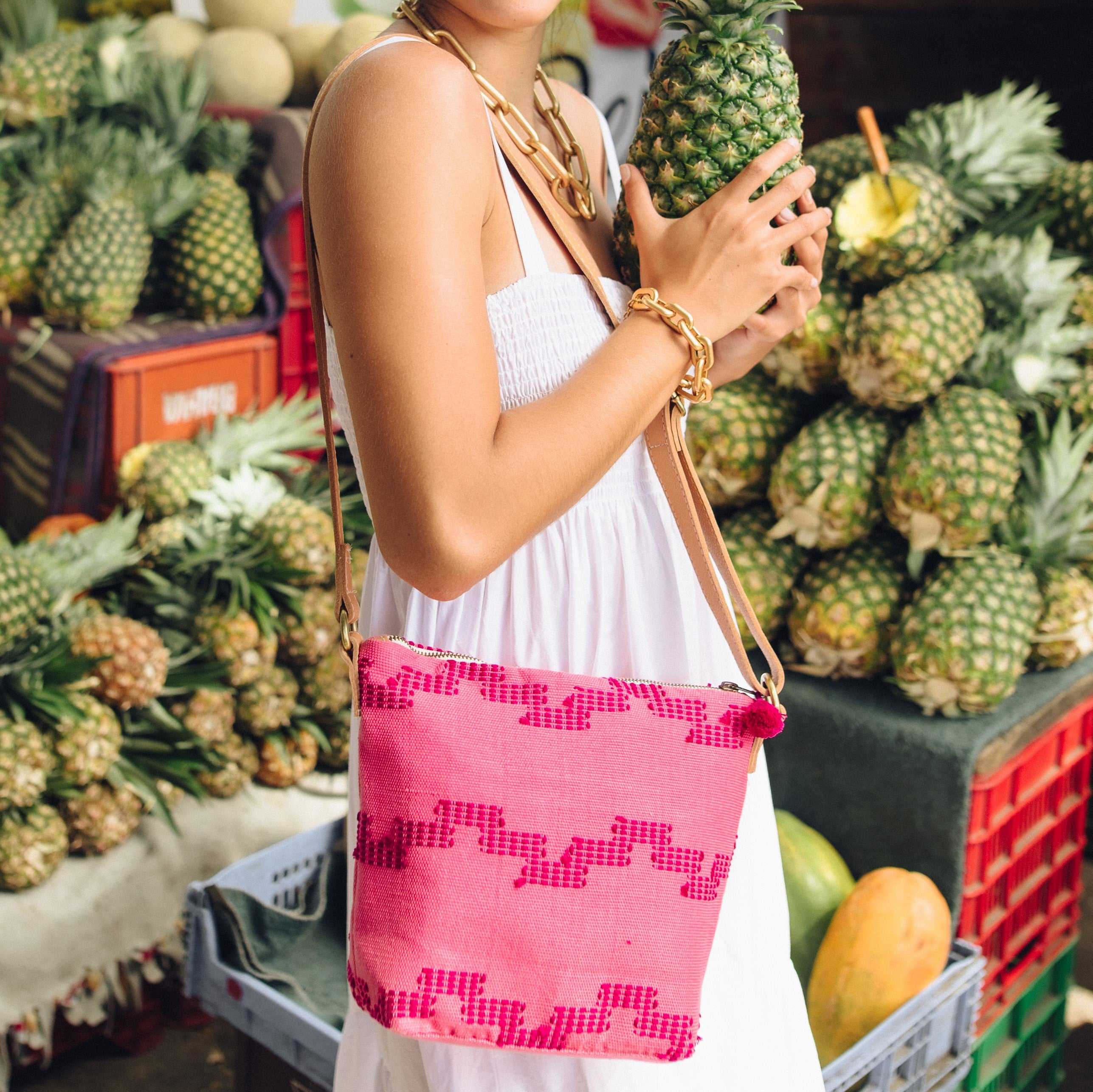 A model wears the hand woven artisan Mini Lidia Crossbody in Pitaya style. The model poses in front of a fruit vendor.