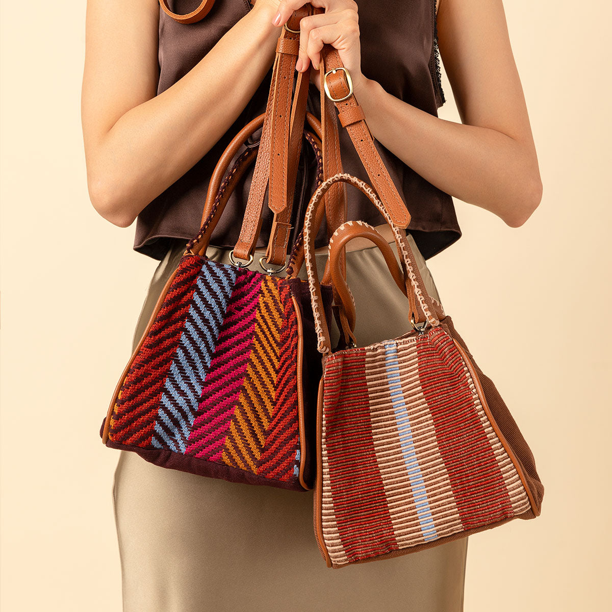 A model holds two Flora Petite Totes in Winter Berry and Chestnut. The Winter Berry has ochre yellow, blue, and red stripes. The Chestnut has vertical brown and tan stripes.