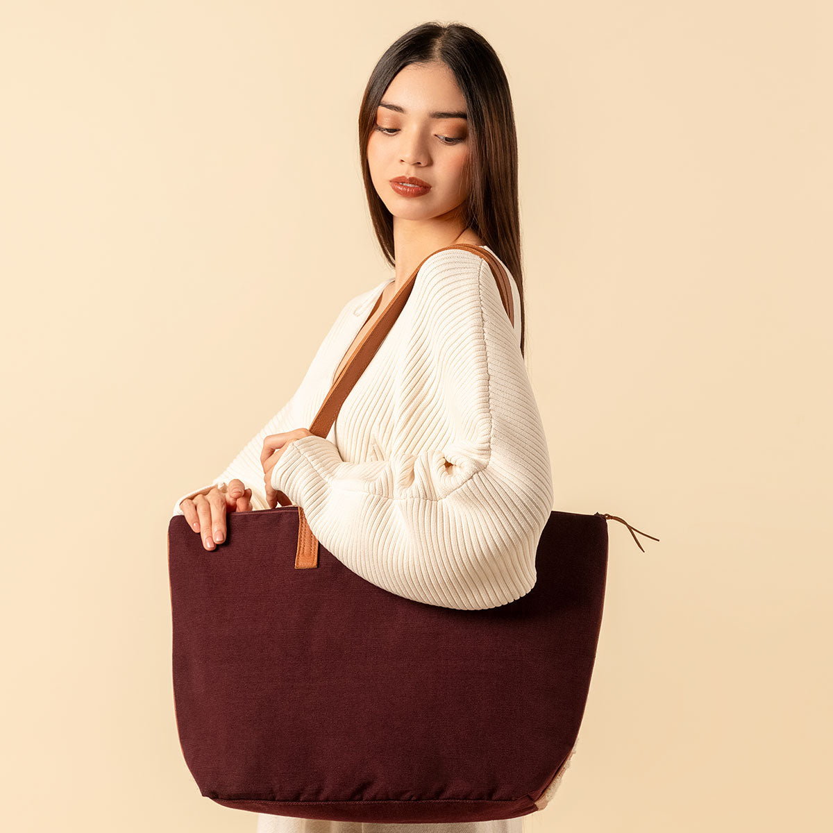 Hand woven artisan Estella Tote in Winter Berry pattern. A model carries the back on her shoulder and looks down. The back of the Estella tote shows in a dark brown solid color. It has leather handles.