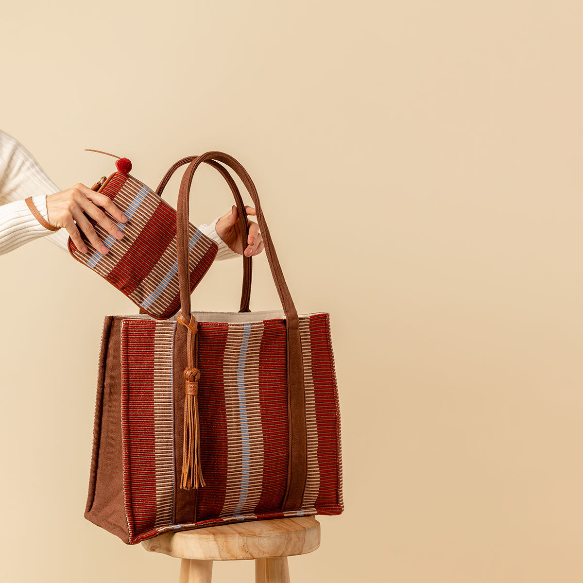 Hand woven artisan Irma Tote and Mini Lily Wristlet in Chestnut color. A model has the leather handle wrapped around her wrist and places the Mini Lily Wristlet into the Irma Tote.