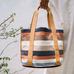 A model holds the Magali Tote in Blue Canyon. The background is a white wall and plants.