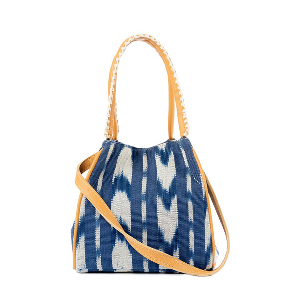 The front of the hand woven artisan Flora Petite Crossbody in Atitlán Hills pattern. It has a detachable leather strap draped diagonally on the front. It has vertical and chevron dark blue and white stripes.  It has leather handles with white embroidery. 