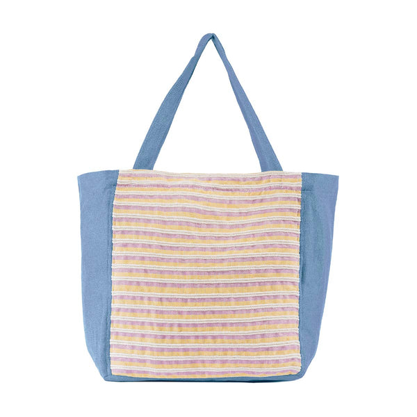 The front of the hand woven artisan Blanca Tote in Cream Soda. The pattern has thin horizontal stripes of pastel yellow, beige, and pink. It is lined in a sky blue fabric and has blue handles.