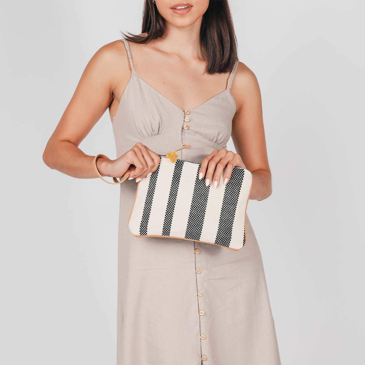 A model holds the hand woven artisan Mini Carolina Clutch in Tourmaline pattern, the leather strap worn on the wrist.