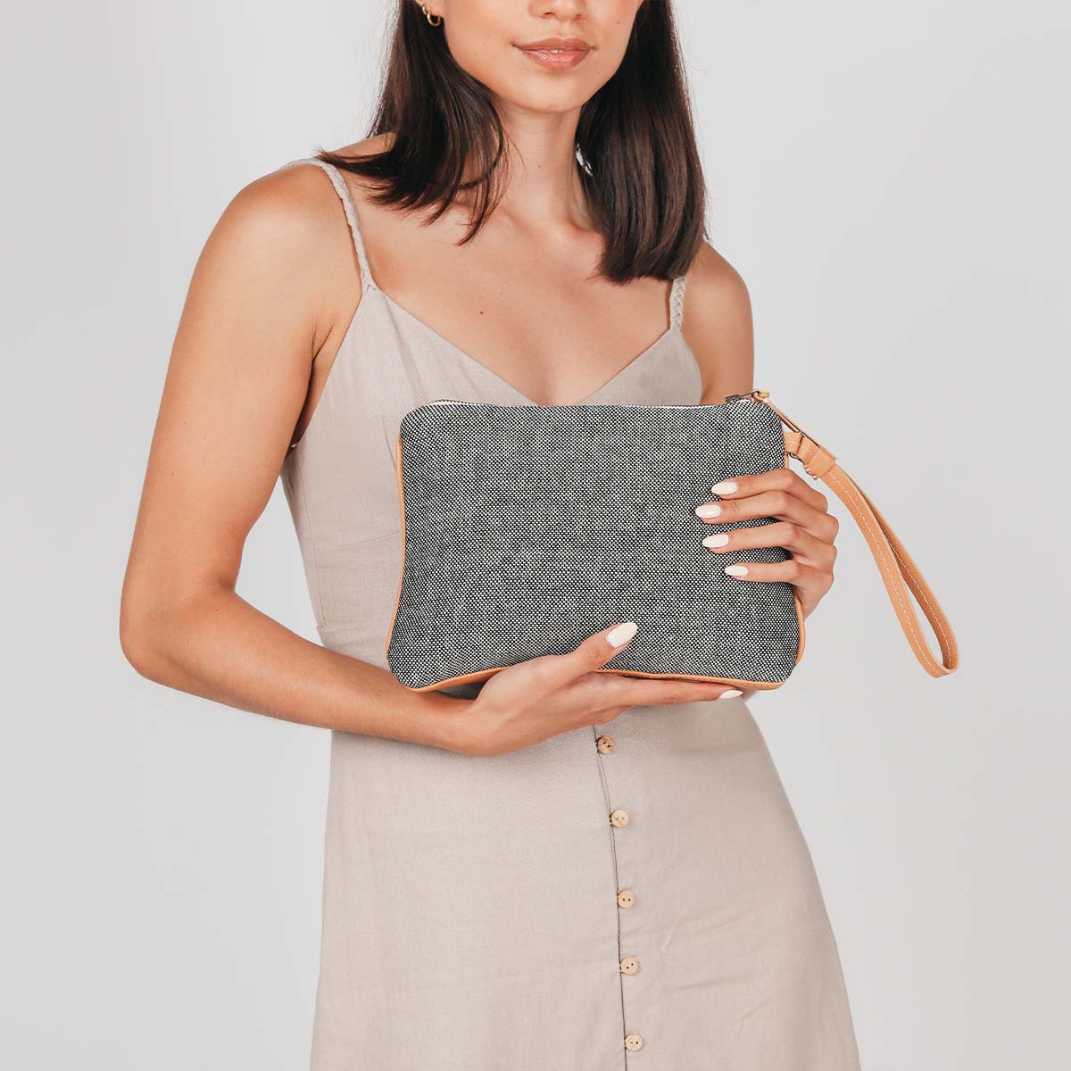 A model holds the hand woven artisan Mini Carolina Clutch in Tourmaline pattern, showing the solid grey back of the bag.