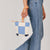 A model wears the hand woven artisan Ofelia Clutch in 90s denim around her wrist. 