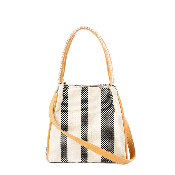 The front of the artisan hand woven Flora Petite Tote in Tourmaline pattern. It has vertical white and black stripes. It has a leather handle with white embroidery and a detachable leather strap hung diagonally across the front.