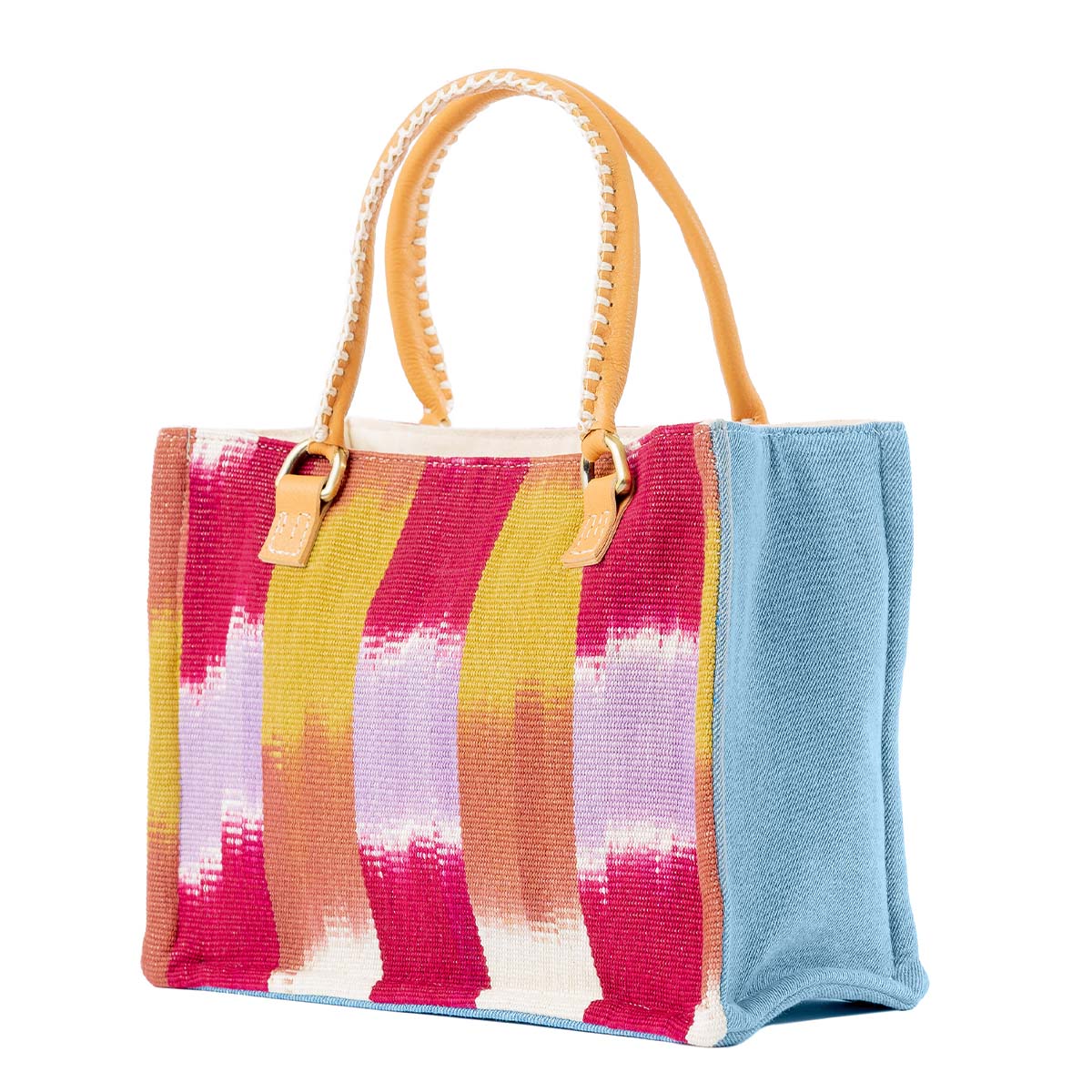 An angle of the Mini Irma Tote in Raspberry Paleta.  It has a flame stitch red, orange, yellow, purple, and white stripes. The sides are sky blue. It has leather handles with white embroidery.