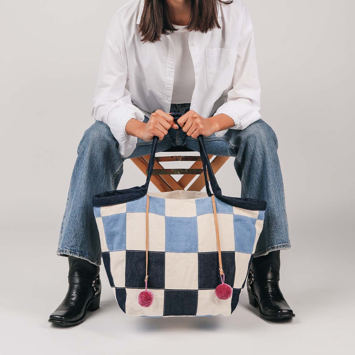 A model sits and holds the artisan hand woven Rosa Tote in 90s Denim. 