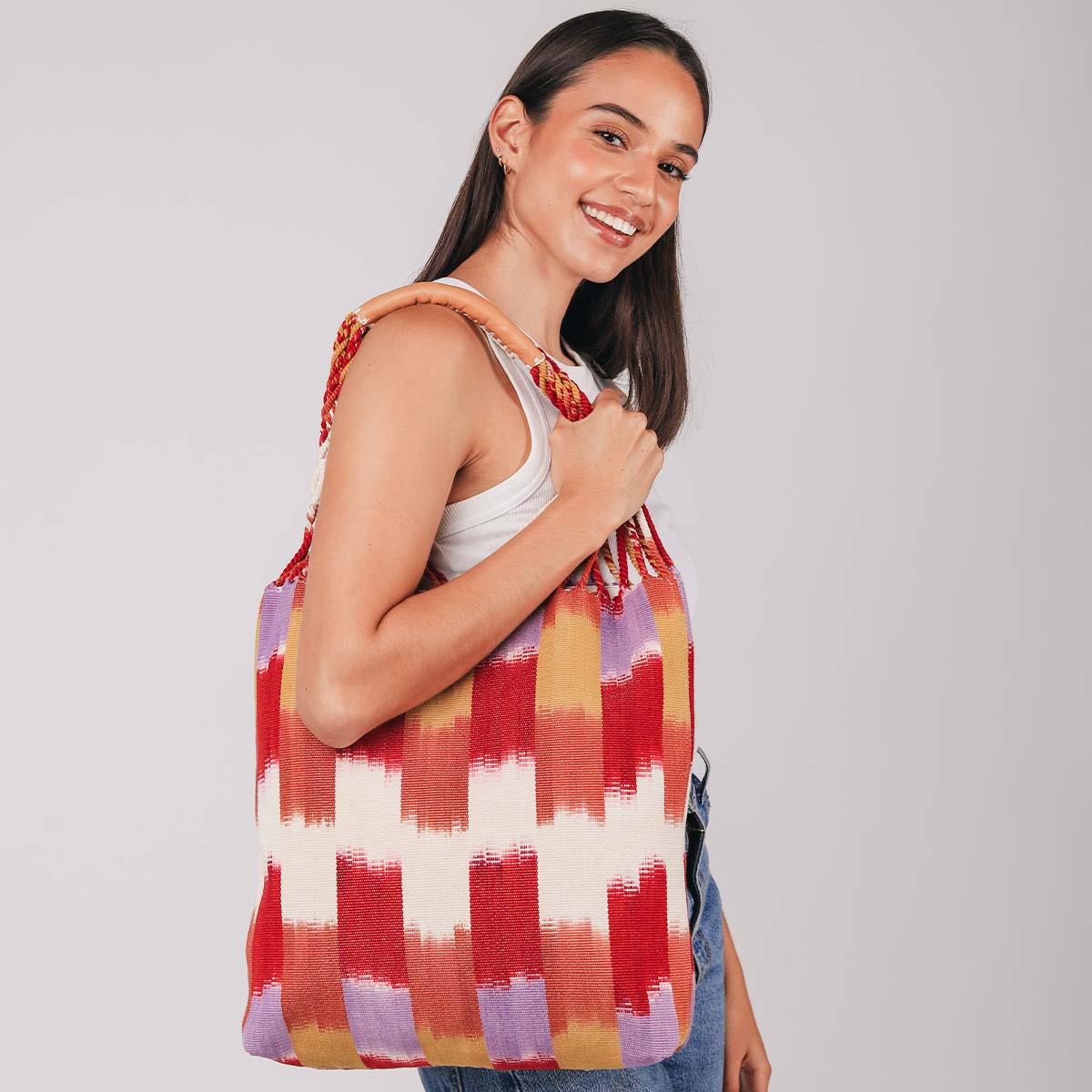 A model smiles at the camera and holds the hand woven artisan Apolonia Tote in Raspberry Paleta over her shoulder.