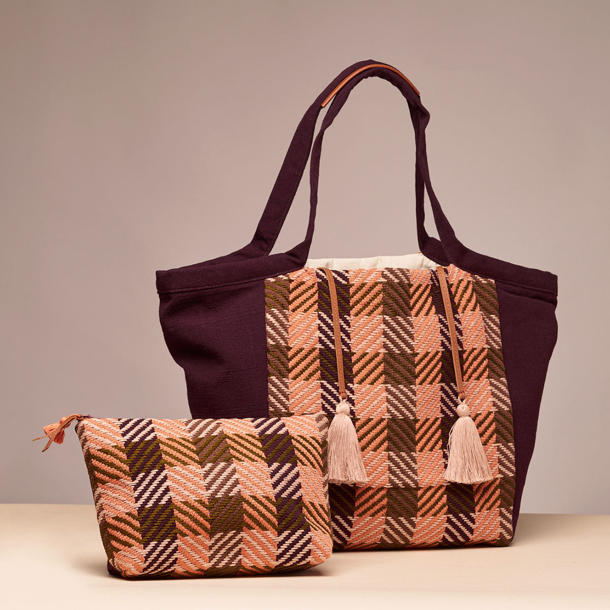 Hand woven artisan Rosa Tote and Cristina Pouch in Moss Weave pattern. The Moss Weave is an orange and olive green plaid grid. The Cristina Pouch is placed in front of the Rosa Tote, both are at slight angles. The Rosa Tote has two pale pink tassels. The background is a beige purple and yellow color.