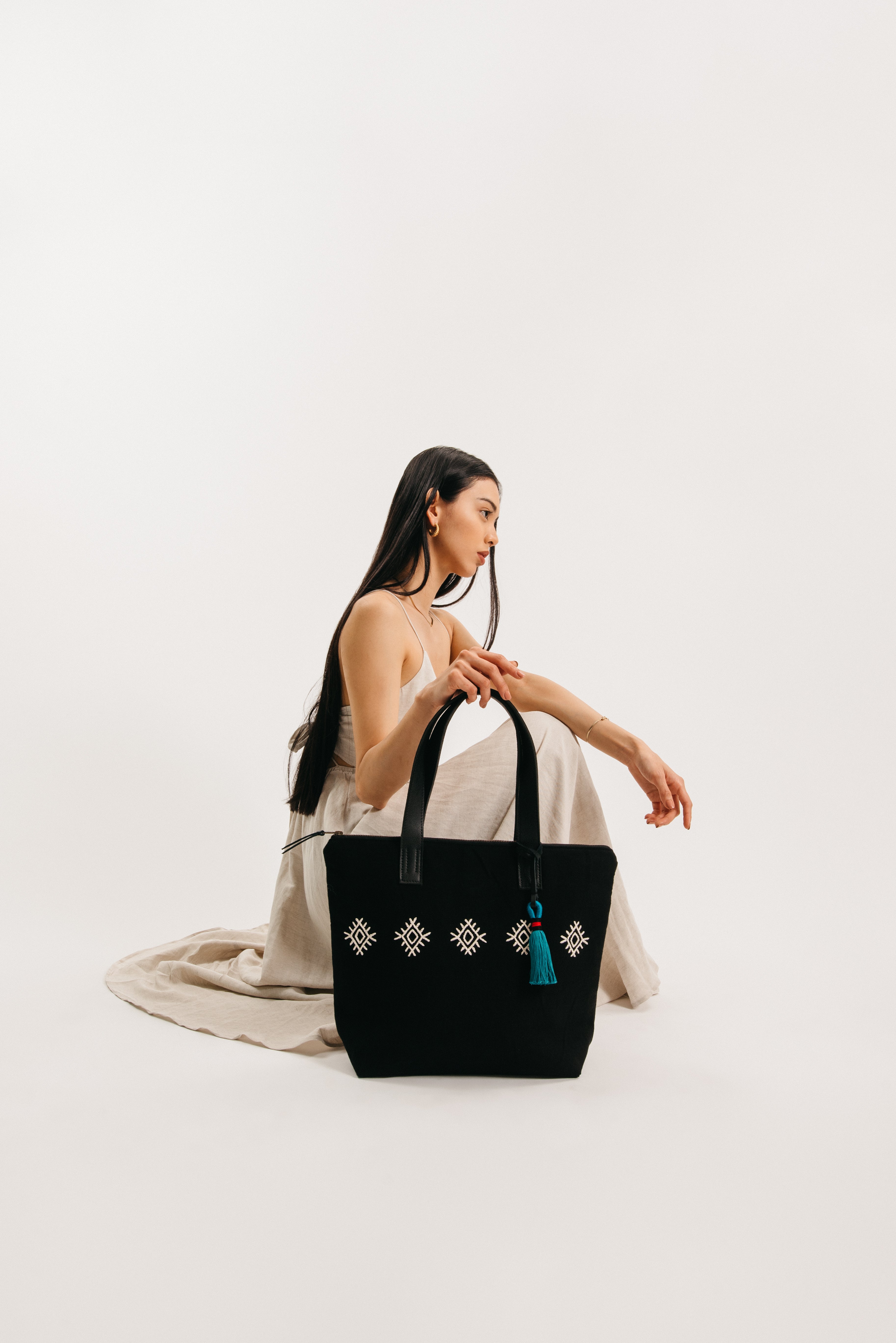 A model holds the Angela Tote with black and white embroidered diamond pattern. It has a phthalo green tassel.