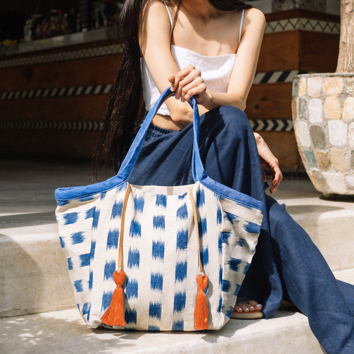 A model sits and holds the hand woven artisan Rosa Tote in Brushstrokes.